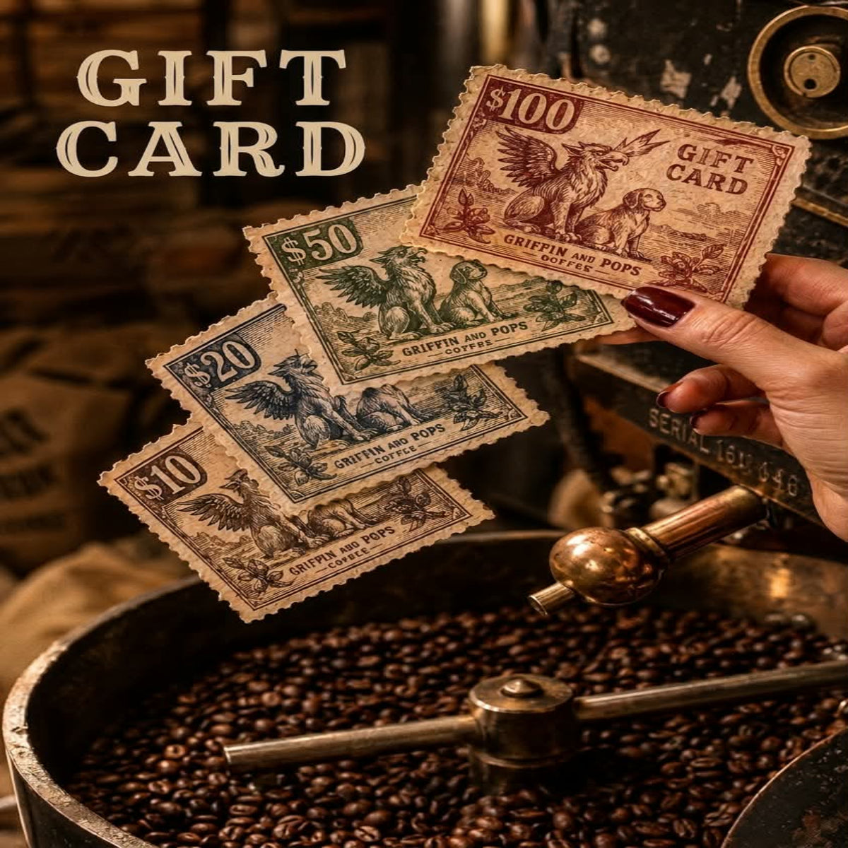 A hand with dark red nail polish holds three vintage-style coffee gift cards above a coffee roaster filled with roasted beans. The cards are labeled $100, $50, $20, and $10 in gold and muted blue-green tones, with the words 'GIFT CARD' printed at the top left.